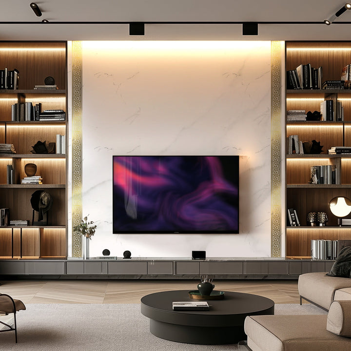 The modern living room features a large TV on Landmark Decors Golden Edge Marble Durable PVC Wall panels, with built-in wooden shelves illuminated by LED lighting. The shelves showcase books, vases, and decor. A round coffee table rests on a beige rug, creating a cozy yet stylish atmosphere.