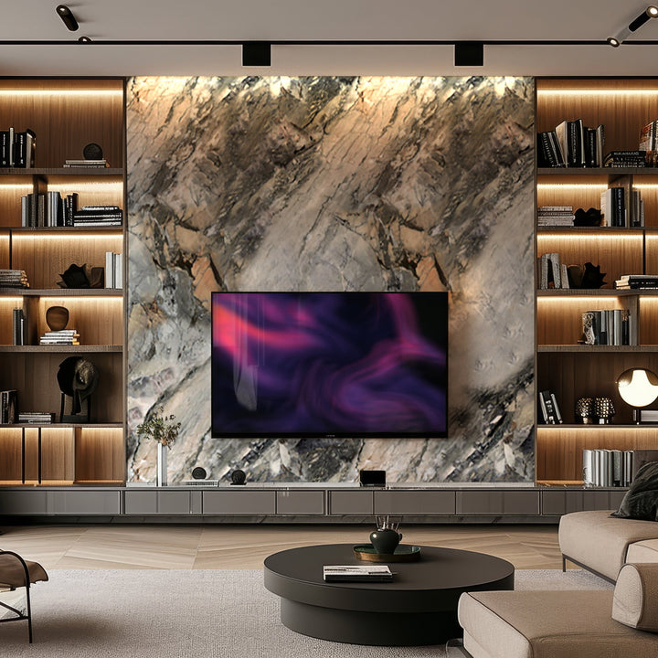 A modern living room with luxurious aesthetics featuring a large Fossil Gray Marble Durable PVC Wall by Landmark Decor, a flat-screen TV, shelves with various items, and a round coffee table in front. Warm lighting highlights the decor, enhancing the contemporary setting.