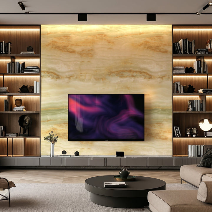 A modern living room features a large, mounted TV on Landmark Decors Opal Forest Marble Durable PVC Wall panels. Wooden shelves with books and decor flank the TV. A round coffee table with a flower vase sits on a plush carpet, while warm lighting enhances the cozy atmosphere.