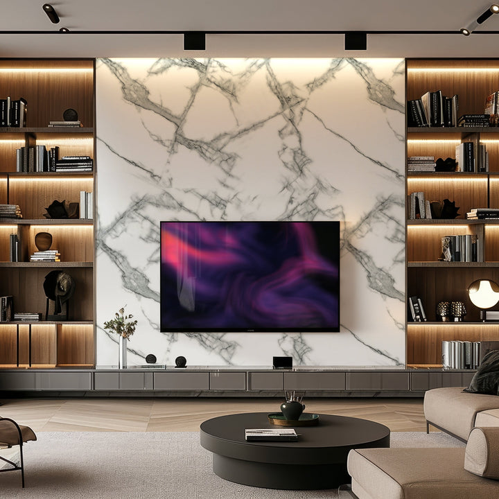 A modern living room showcases a large TV mounted on Landmark Decors Silver Frost Marble Durable PVC Wall panels. Wooden shelves with decor items flank the TV, while a round coffee table rests on a beige rug. Soft lighting enriches the cozy ambiance, ensuring stylish and durable elegance.