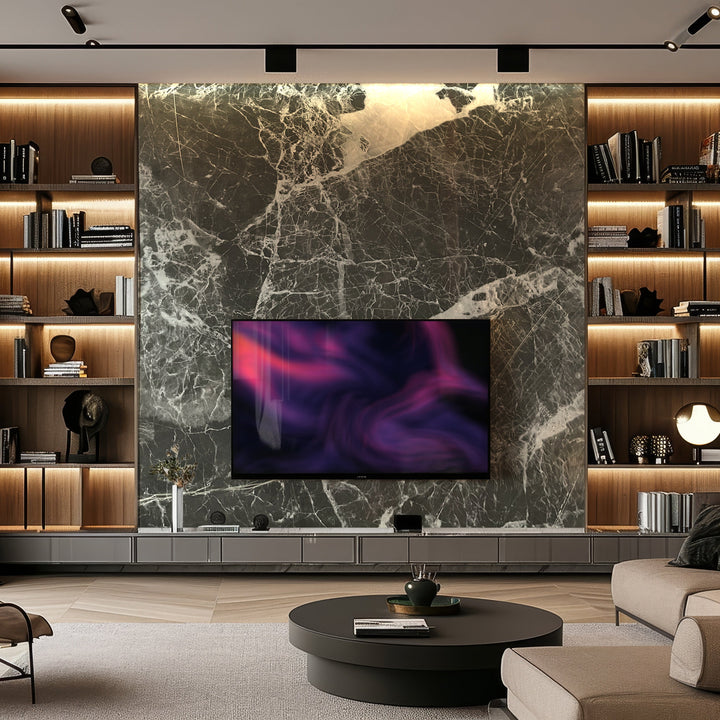 A modern living room showcases a large TV mounted on Landmark Decors Shadow Mist Marble Durable PVC Wall panels, offering durability and elegance. Flanked by wooden shelves with books, a round coffee table sits before a low cabinet beneath the TV, all enhanced by warm lighting for coziness.