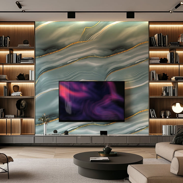 In a modern living room, a large TV sits on a wall adorned with Landmark Decors Serene Glacier Marble Durable PVC Wall panels, showcasing a wavy green and gold abstract design. Shelves hold books and decor items, while a round coffee table adds to the luxurious ambiance of this contemporary space.