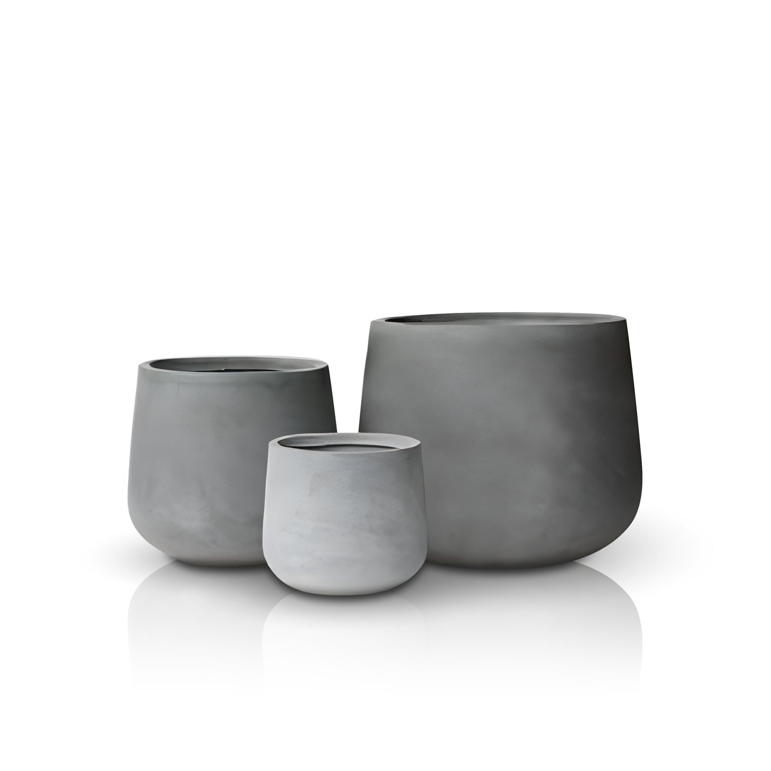 A trio of Fortezza Planters by Landmark Decor, in matte gray with a smooth minimalist design, sit luxuriously on a reflective white surface. The largest planter is positioned to the right, with the two smaller ones partially overlapping it on the left.