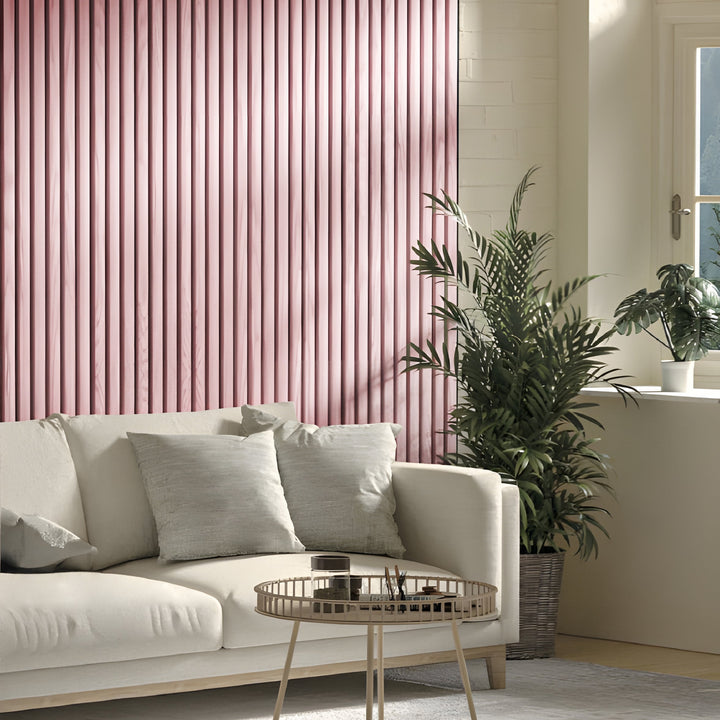 A cozy living room features a light sofa with gray cushions. A Landmark Decor Pink WPC Fluted Slat Wall Panel adds warmth. Potted plants and a round coffee table enhance the airy feel, while natural light streaming through a window highlights the stylish interior panels.