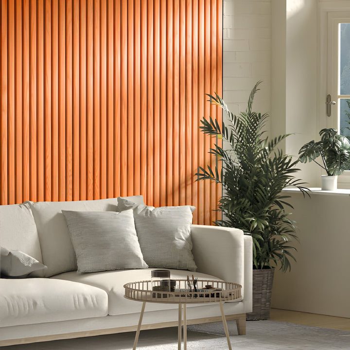 A modern living room boasts a white sofa with two gray cushions and a round coffee table. Orange WPC Fluted Slat Wall Panels from Landmark Decor accent the walls, creating a bold backdrop, as sunlight highlights lush potted plants by the window.